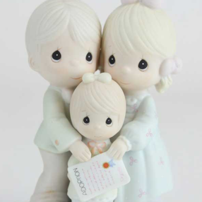 Precious Moments figurine depicts a mother and father adopting a little girl.