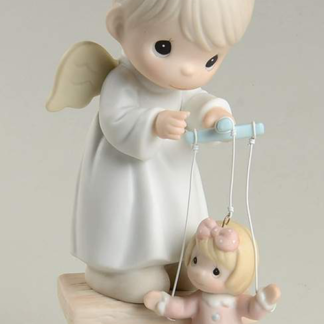 Precious Moments figurine depicts an Angel standing on a stool working a marionette puppet.