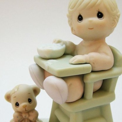 porcelain figurine of A Baby In A Highchair With A Bowl And A Teddy Bear At Her Feet.