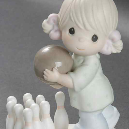 Porcelain figurine depicts a girl holding a bowling ball with bowling pins.