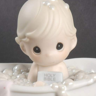 Porcelain figurine of child in bathtub filled with bubbles, holding bible